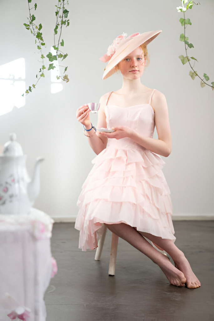 Young woman in a pastel pink ruffled dress and wide-brim hat enjoying a tea party